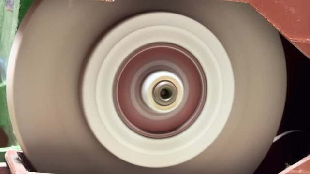 A motorized abrasive wheel rotates at high speed against its housing. The rapid motion generates a consistent, mechanical whirring sound and a low-frequency hum.