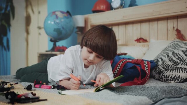 Young boy creating with toys, Child is happily drawing while laying on bed surrounded by art supplies and toys