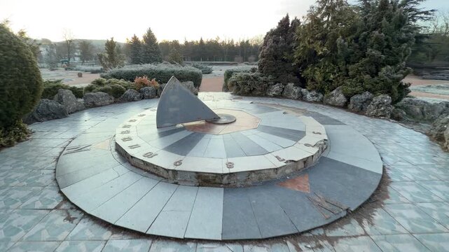 A monumental sundial sits in a peaceful, frost-covered garden surrounded by dense evergreens. The cool morning air and stone architecture create a feeling of timeless calm and solitude