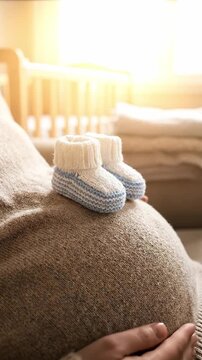 Pregnant woman belly with baby bootie knit maternity pregnancy, newborn nursery crib at home, baby shoe near belly for maternity pregnancy nursery setup