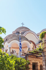 White domed orthodox church with a Greek flag under a clear blue sky