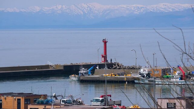 残雪期の山と虻田漁港　赤い灯台と湾に出ていく漁船　春の北海道