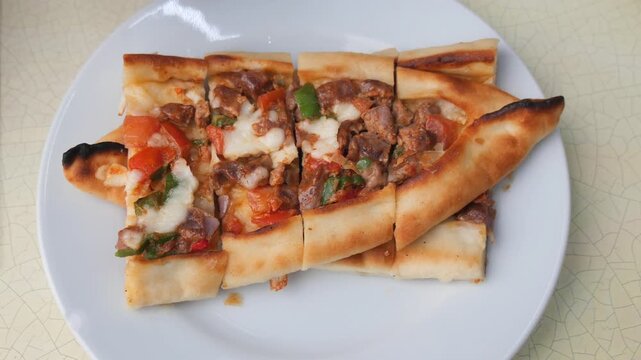 Hand picks delicious piece of Turkish pide with meat and cheese topping.