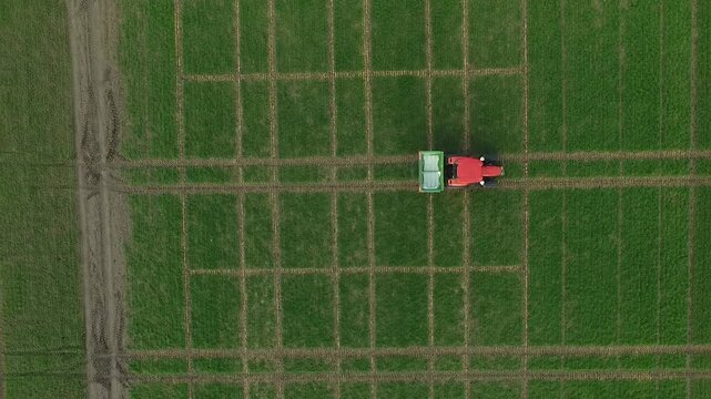 High altitude top-down aerial view of tractor spreading mineral fertilizer across large grid of agricultural trial plots, emphasizing field structure and precision farming