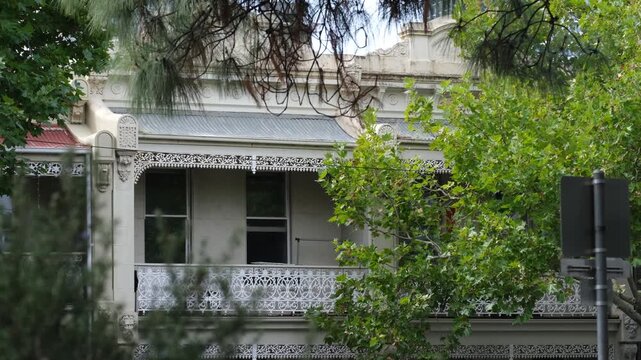 Ornate heritage terrace house with decorative iron lacework verandah in a leafy neighborhood, west Melbourne, Australia. Historic residential architecture, Victorian-era design, inner-city character.