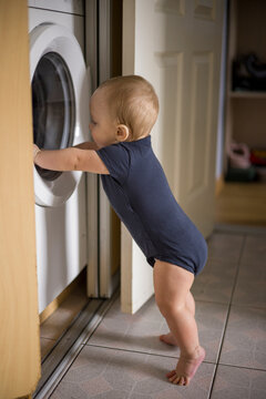 Inquisitive Child Exploring. Toddler Engaging With Washing Machine. Young Child Reaching Into Laundry Drum Playfully. Baby In Navy Outfit Exploring Laundry Area Happily verical