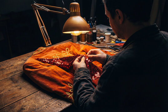 Man hands sewing red sequins onto a luxurious velvet jacket