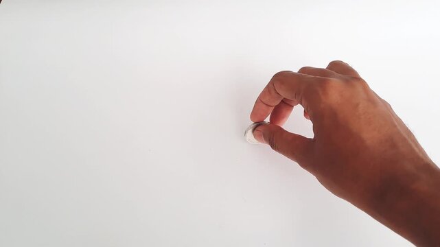 Horizontal shot of an Asian man's hands spinning a silver coin on a white minimalist background. This footage captures the concept of probability. PAMEKASAN, INDONESIA - APRIL 1, 2026