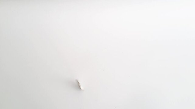 Horizontal shot of an Asian man's hands spinning a silver coin on a white minimalist background. This footage captures the concept of probability. PAMEKASAN, INDONESIA - APRIL 1, 2026