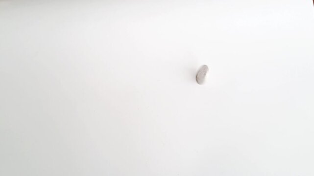 Horizontal shot of an Asian man's hands spinning a silver coin on a white minimalist background. This footage captures the concept of probability. PAMEKASAN, INDONESIA - APRIL 1, 2026