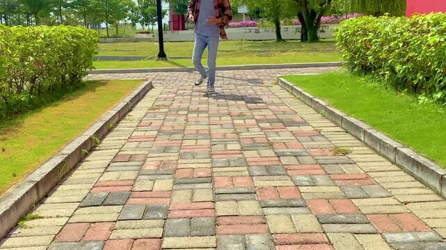 Man leisurely walks on brick path through a park near green bushes during bright daylight