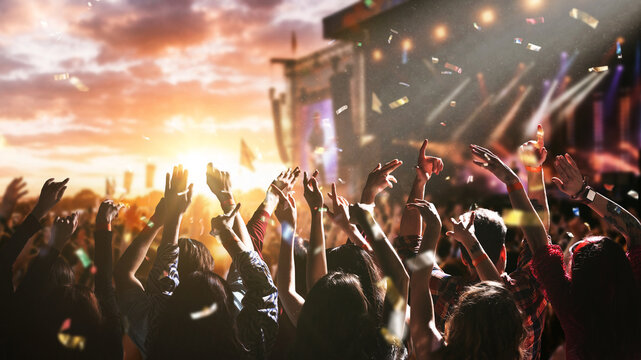 Large crowd dancing and celebrating at music festival stage with confetti and sunset sky. Concept of high energy event visuals, entertainment marketing, festival branding content, audience engagement