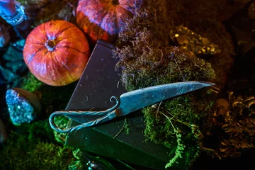 knife sits on a black box surrounded by pumpkins and moss. Various decorative items are scattered around. scene has a low light setting with colored lighting effects © angel_nt