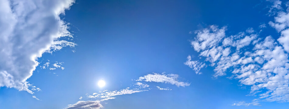 A panorama of cumulus clouds against a blue sky. A summery, serene landscape. The cloud's smooth movement copy space for banner text. Clear background with tiny white fluffy cloud.