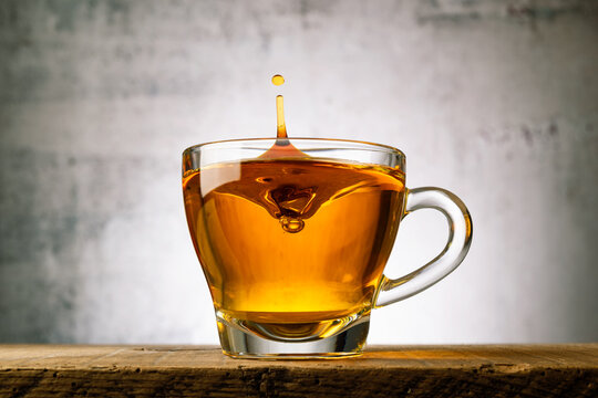 Glass cup of tea on wooden table with splashing drop.