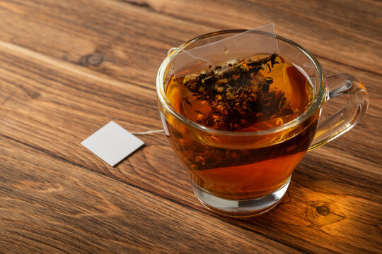 Glass cup of tea on wooden table with tea bag inside.