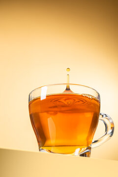 Glass cup of tea with splashing droplet on yellow background