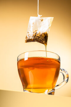 Glass cup of tea with dripping tea bag on yellow background