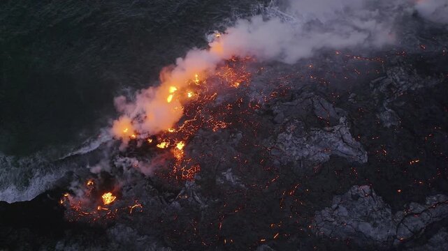 Aerial view of molten lava flowing into the ocean, contrasting violently with the dark rock and emitting plumes of smoke, Piton de la Fournaise, Saint-Benoit, Reunion.