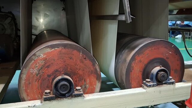 Part of an industrial machine, most likely a paper production or sheet material processing machine. Industrial Machine: This image shows a large, rusty roller used to continuously move sheets of mater
