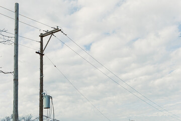 Fototapeta premium Electricity poles stand in the field under a cloudy sky with power lines connecting them to the grid in a rural area during the day