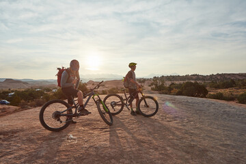 Fototapeta premium Man, friends and mountain bike with rest at sunset for break, perspective or outdoor for fitness. People, bicycle and space in sky for view in summer for exercise, wellness and cycling in countryside