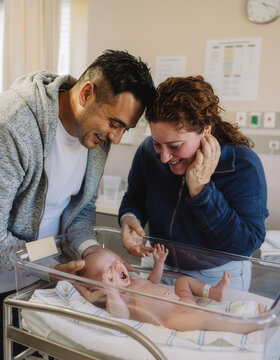 Emotional new parents crying tears of joy while looking at their newborn baby in a hospital bassinet. Medium shot, authentic documentary style, natural indoor lighting