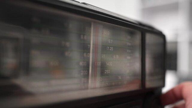Close-up shot of boombox radio dial. Hand turns tuning knob, adjusting the orange indicator as it scans various radio frequencies, searching channel. Tuning frequency analog radio station