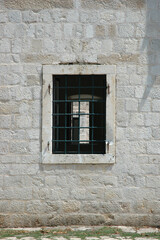 Fototapeta premium A traditional window with a white stone frame and green iron bars is set into a weathered light stone wall in the town of Ston