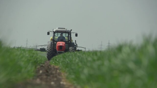 Tractor spraying crops while moving across agricultural field with camera tracking from side, showcasing mechanized crop treatment and large scale farming operations