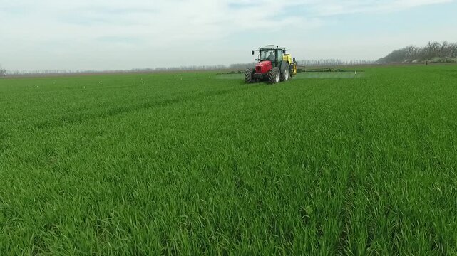 Aerial orbit view of tractor spraying crops on agricultural field, capturing dynamic movement and large scale mechanized farming during crop treatment process