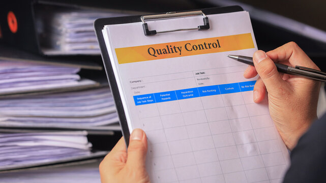 Focused professional holding clipboard with quality control document and pen inspecting paper folder stack in corporate business office