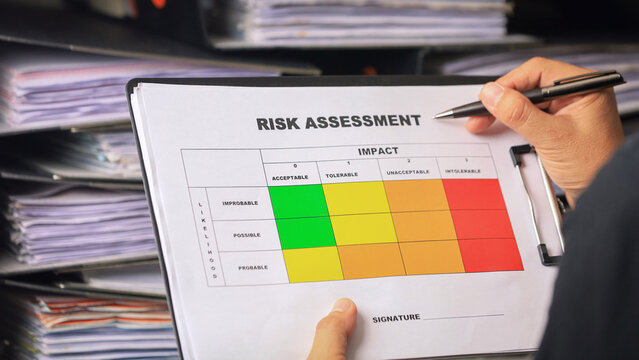 Focused professional evaluating risk assessment matrix on clipboard in busy office setting holding pen to review safety protocols
