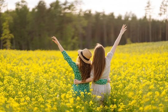 Two cheerful friends in dresses are having fun in a blooming field, bathed in sunlight. The young women pose outdoors, enjoying nature. Concept: style, fashion, and friendship.