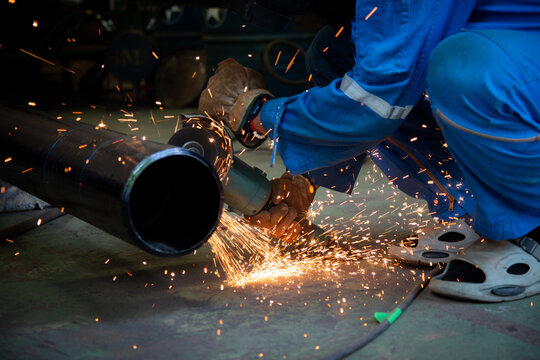 Worker cutting steel pipe with abrasive saw without proper safety footwear, highlighting unsafe working conditions, flying sparks, and potential workplace hazards in industrial environment.