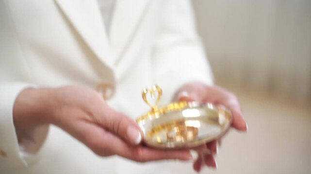 Priest holding a small golden plate with two shiny wedding rings, ready for a traditional marriage ceremony