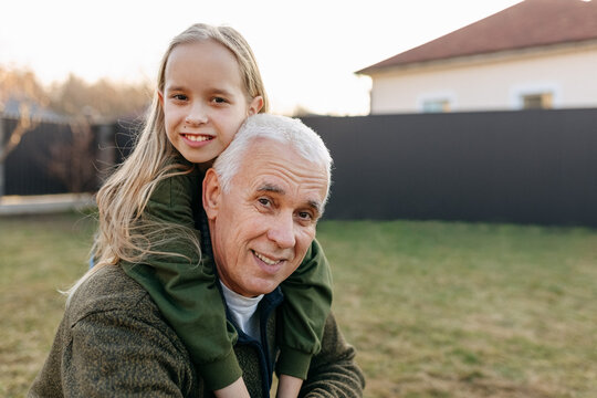 Granddaughter piggyback ride on grandfather outdoors in backyard