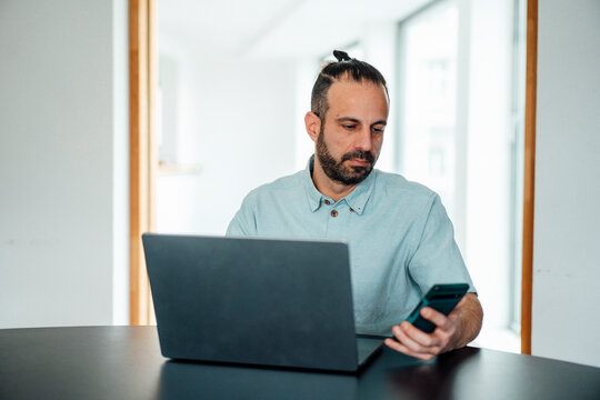 Developer working on laptop and smartphone in a bright home office