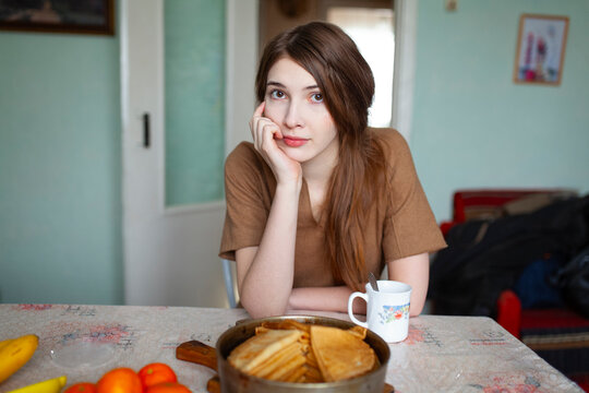 Young woman in brown dress having lunch with pancakes in kitchen