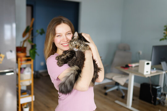Smiling woman at home hugging cat in pink t-shirt indoors