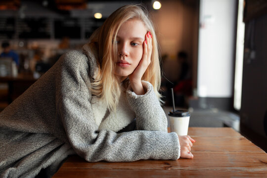 Thoughtful woman in a cafe resting hand on face with drink