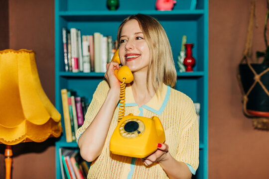 Smiling woman holding retro yellow phone in stylish home interior