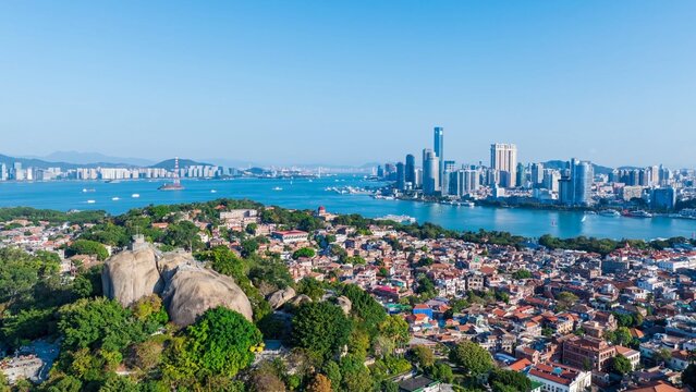Aerial view of Gulangyu Island and Xiamen skyline under blue sky with white clouds, Fujian, China.Stunning drone shot showcasing Gulangyu Island (UNESCO) and the modern Xiamen city across the sea.