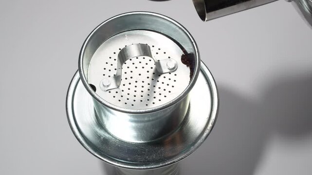 Close up footage of pouring boiling water into a traditional Vietnamese metal phin coffee filter on a white background. Bright commercial brewing video.