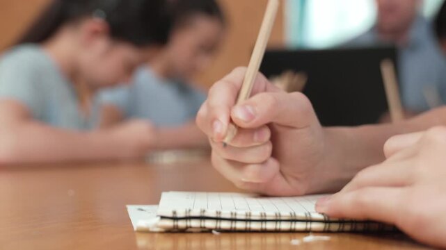 Closeup of student hand taking a note while girl ask teacher a question. Diverse student learning and study with smart happy instructor in classroom. Focus on hand. Blurring background. Edification