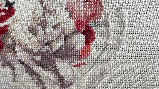 Floral cross-stitch embroidery in progress with a needle and white thread on canvas. Zoom out.