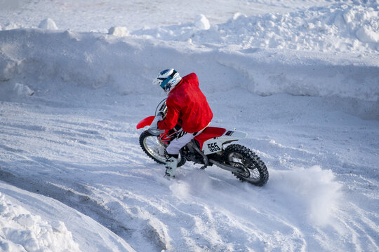 Motocross rider on dirt bike navigating rutted snow track between high snow banks during winter race