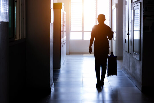 Janitor woman holding mop in hallway office building or walkway after school or classroom for clean floor. Silhouette housekeeper working job with sun light background.