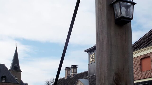 Historic brick buildings with a clock tower and lamp post are shown outdoors under a partly cloudy sky in a quiet street setting.