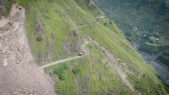 Aerial view of a single truck crossing a massive, active landslide zone on a Himalayan mountain road.